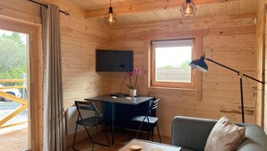L’intérieur chaleureux d’un chalet avec une table à manger en bois, des chaises, un canapé, un téléviseur fixé au mur et une fenêtre donnant sur l’extérieur.