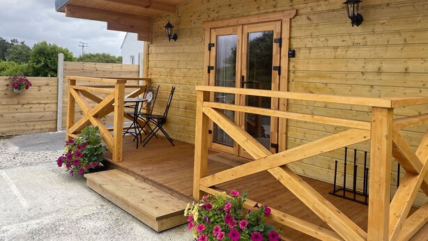 Une cabane en bois avec une véranda, une table et des chaises, et un paillasson.