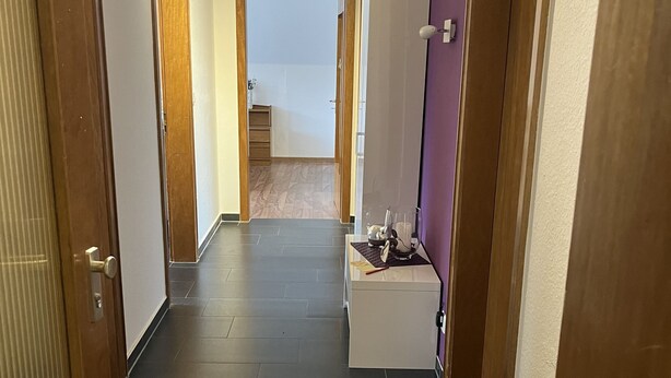 A hallway with dark tiled flooring, wooden doors, and a purple wall. - Apartment Geronimo (Werne)