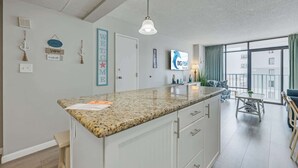 A modern kitchen with a granite countertop, white cabinetry, and a hanging light fixture. - Sand Dunes Resort 7th Floor Direct Oceanfront Pool (Myrtle Beach)