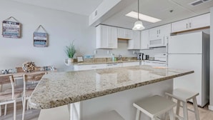 A modern kitchen with white cabinetry, a granite countertop, and bar stools. - Sand Dunes Resort 7th Floor Direct Oceanfront Pool (Myrtle Beach)