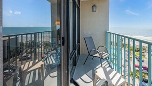 A balcony with a view of the beach, a chair, a table, and a lamp. - Sand Dunes Resort 7th Floor Direct Oceanfront Pool (Myrtle Beach)