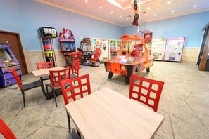 Une salle d’arcade proposant divers jeux, des chaises rouges et des tables.