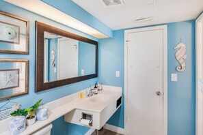A bathroom with a white sink, a large mirror, and a door with a seahorse decoration. - Sand Dunes Resort 7th Floor Direct Oceanfront Pool (Myrtle Beach)