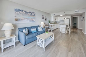 A modern living room with a blue sofa, a white coffee table, and a kitchen in the background.