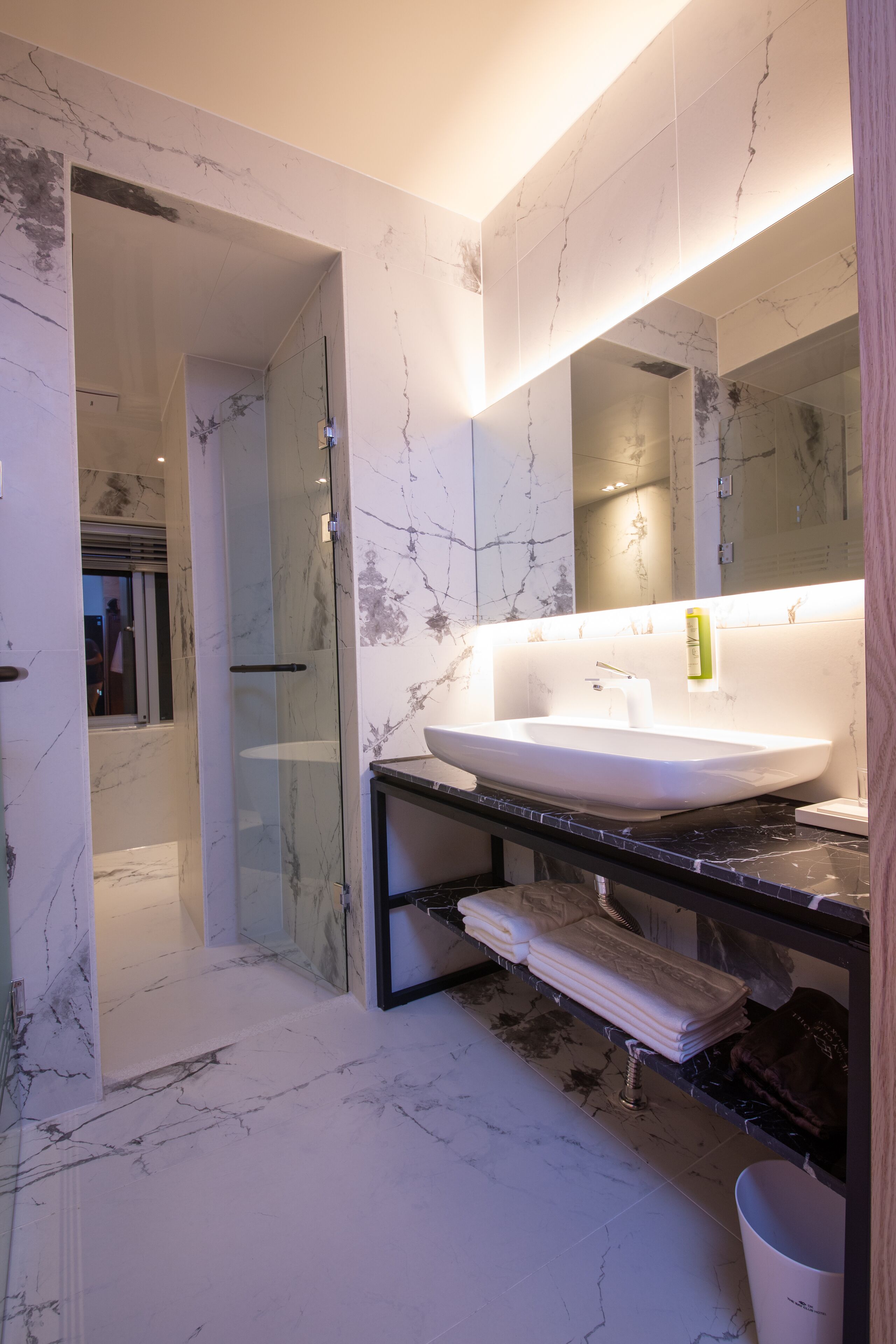 A modern bathroom with a large marble sink, a glass shower enclosure, and a vanity with towels.