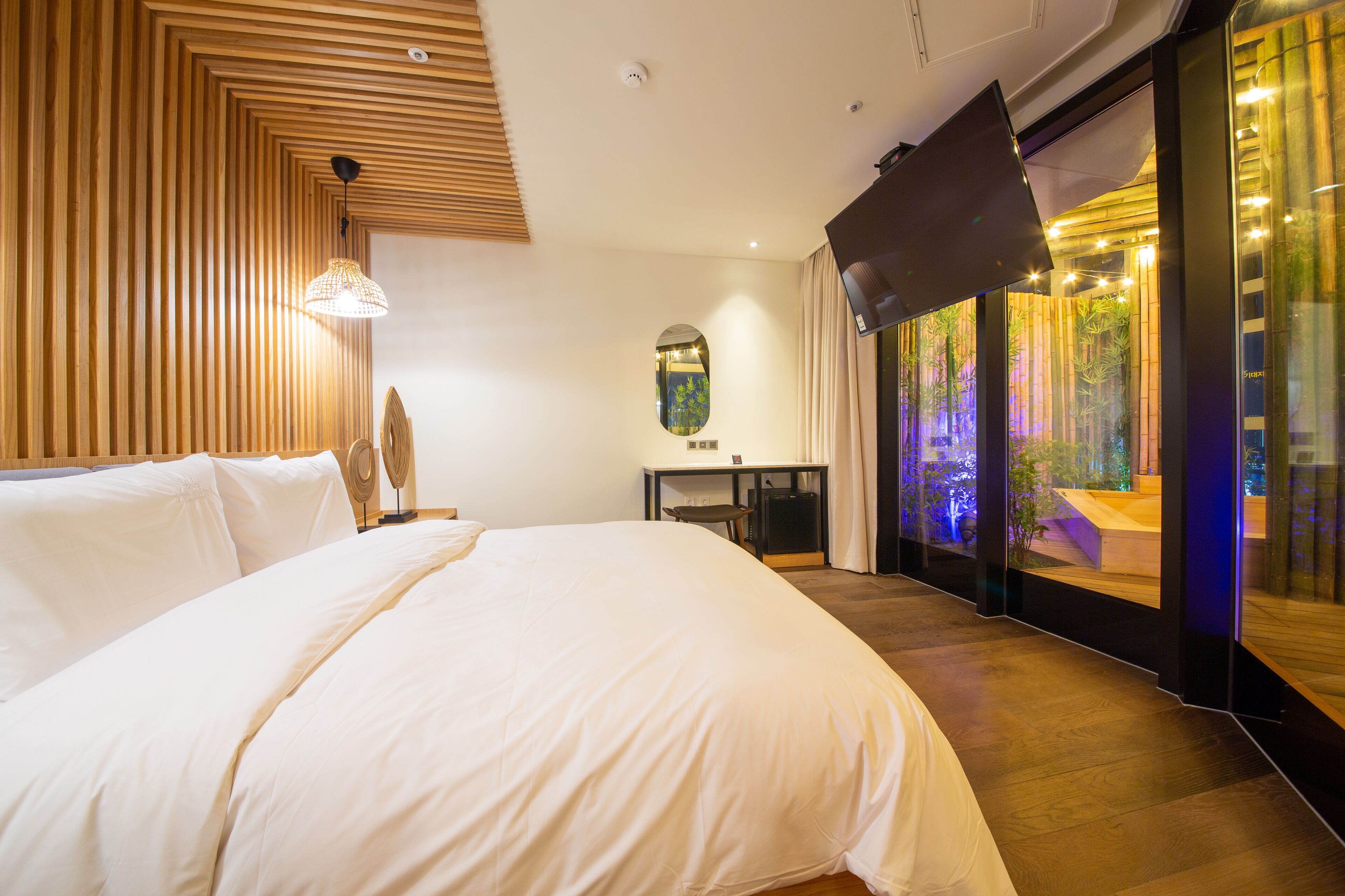 Quarto de hotel moderno com uma cama grande, uma escrivaninha e vista para plantas em vasos através de uma porta de vidro.