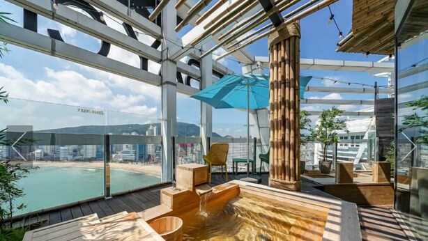 A wooden deck with a hot tub, chairs, and a large umbrella. - Gwanganri The Club hotel (Busan)