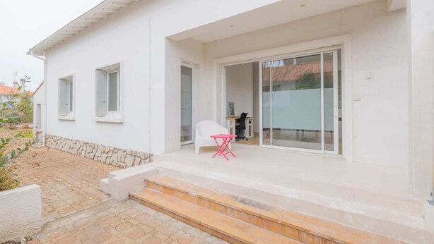 A white building with a covered patio, a small table, and a chair. - Villa Luxe Plages et Commerces à Pieds (carnac)