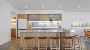 A modern kitchen with a central island, wooden bar stools, and a refrigerator. - Casa Bella on Beach in Cowes (Cowes)