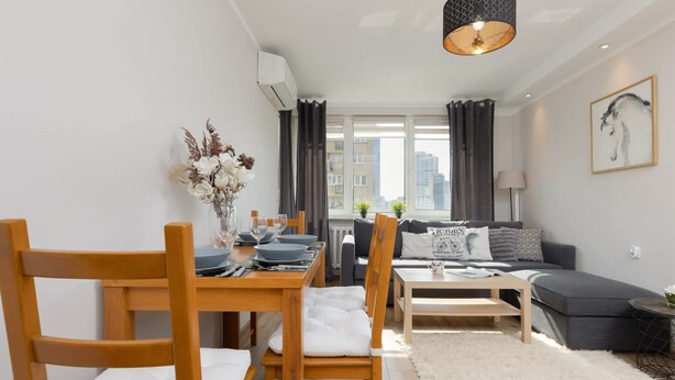 A modern living room with a dining area, featuring a sofa, a coffee table, and a dining table with chairs. - Comfortable Apartment in the Center | Balcony and Air Conditioning (Warszawa)
