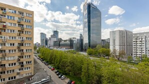 A multi-story residential building with balconies, a parking lot, and a modern skyscraper in the background. - Comfortable Apartment in the Center | Balcony and Air Conditioning (Warszawa)