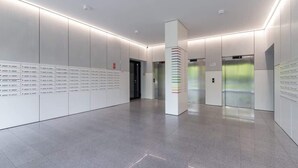 Un hall d’ascenseur moderne, doté d’un design épuré et minimaliste, avec un pilier central orné d’un motif rayé coloré et une rangée d’ascenseurs de chaque côté.