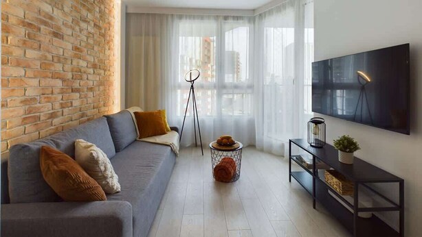 Un salon moderne avec un canapé gris, une table basse ronde, un meuble TV noir et un mur en briques.