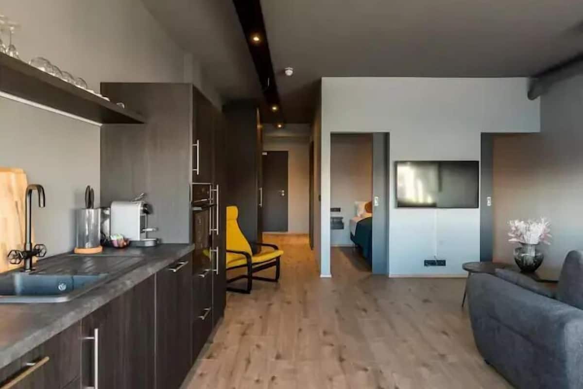 A modern kitchen with dark cabinets, a yellow chair, and a dining area with a grey sofa.