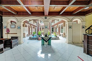 A spacious lobby with a central table, multiple arches, and potted plants. - OYO 91596 Hotel Rajadani (Yogyakarta)