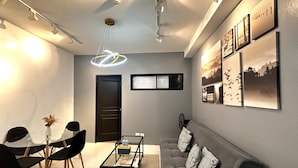 A modern living room with a grey sofa, black chairs, a glass coffee table, and wall-mounted artwork. - Malate Bayview Mansion (Manila)