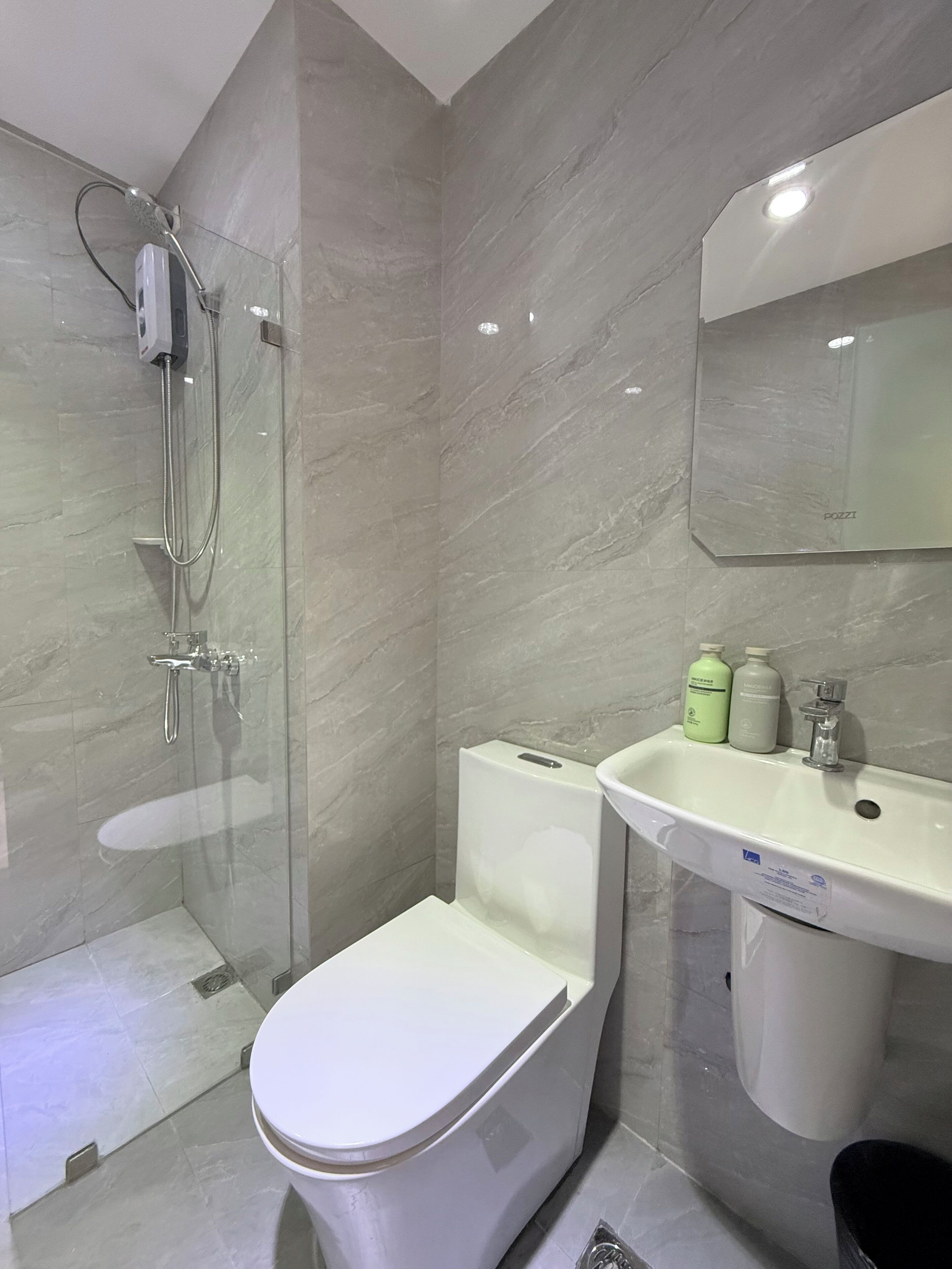 A modern bathroom with a glass-enclosed shower, a white toilet, and a sink with toiletries.