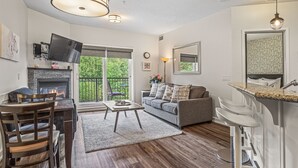 A modern living room with a fireplace, a sofa, a coffee table, and a dining area with chairs. - Rocky Mountain Haven - Mountain Views | Pool & Waterslide! (Canmore)