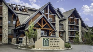 A multi-story building with a stone facade and wooden accents, labeled as Grande Rockies Resort. - Rocky Mountain Haven - Mountain Views | Pool & Waterslide! (Canmore)