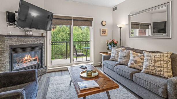 A living room with a fireplace, a flat-screen TV, a sofa, and a coffee table. - Rocky Mountain Haven - Mountain Views | Pool & Waterslide! (Canmore)