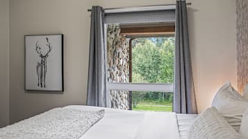 A bedroom with a large bed, a framed deer artwork, and a window with a stone wall view.