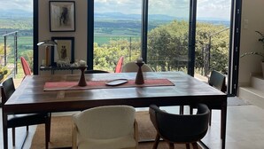 Un comedor con una mesa, sillas, un ventilador de techo y ventanas amplias con vistas al campo.