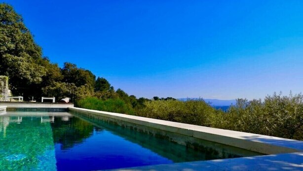 Una piscina rectangular con agua cristalina azul, rodeada de exuberante vegetación y árboles.