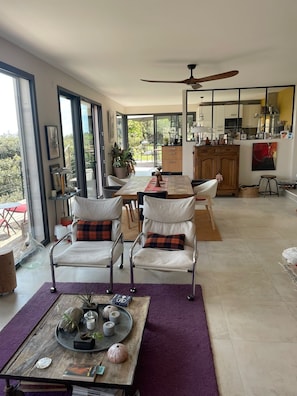 Un vaste espace de vie comprenant une table à manger, deux fauteuils, une table basse agrémentée d’objets décoratifs et une vue sur l’extérieur.