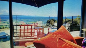 Un balcón con vista al océano, mobiliario rojo y un paraguas grande.