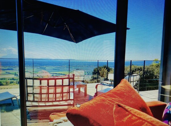 A balcony with a view of the ocean, red furniture, and a large umbrella.