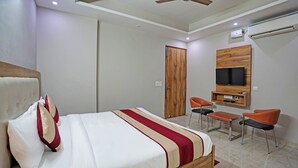 A modern hotel room with a large bed, a TV mounted on the wall, a desk, two chairs, and an air conditioning unit. - Hotel Royal Rosette (New Delhi)