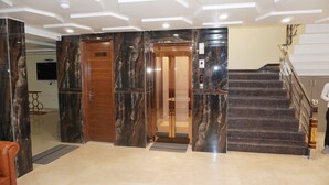 A lobby with a marble reception desk, a wooden door, an elevator, and a staircase with a handrail. - Hotel Royal Rosette (New Delhi)