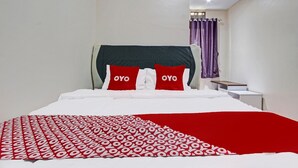 Habitación de hotel con cama, ropa de cama blanca, manta con estampado rojo y blanco, dos almohadas rojas con el texto 