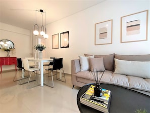 Un salon moderne avec un canapé blanc, des fauteuils noirs, une table à manger et une table basse sur laquelle sont posés des magazines.