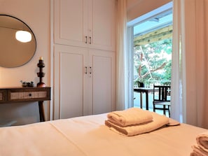 Une chambre à coucher comprenant un lit, une table de chevet avec un miroir, une commode et une vue sur l’extérieur par une fenêtre.