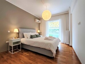 Une chambre à coucher moderne avec un lit, des tables de chevet, un luminaire suspendu et une fenêtre avec des rideaux.