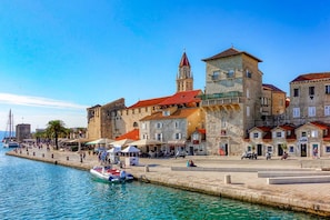A waterfront promenade with stone buildings, a prominent tower, and a small boat docked at the pier. - A3 apt With Balcony and sea View, 3 min to Beach (Trogir)