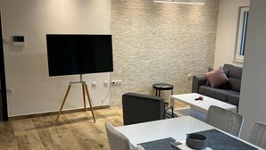 A modern living room with a flat-screen TV on a stand, a dining area with a white table and chairs, and a grey sofa. - A3 apt With Balcony and sea View, 3 min to Beach (Trogir)