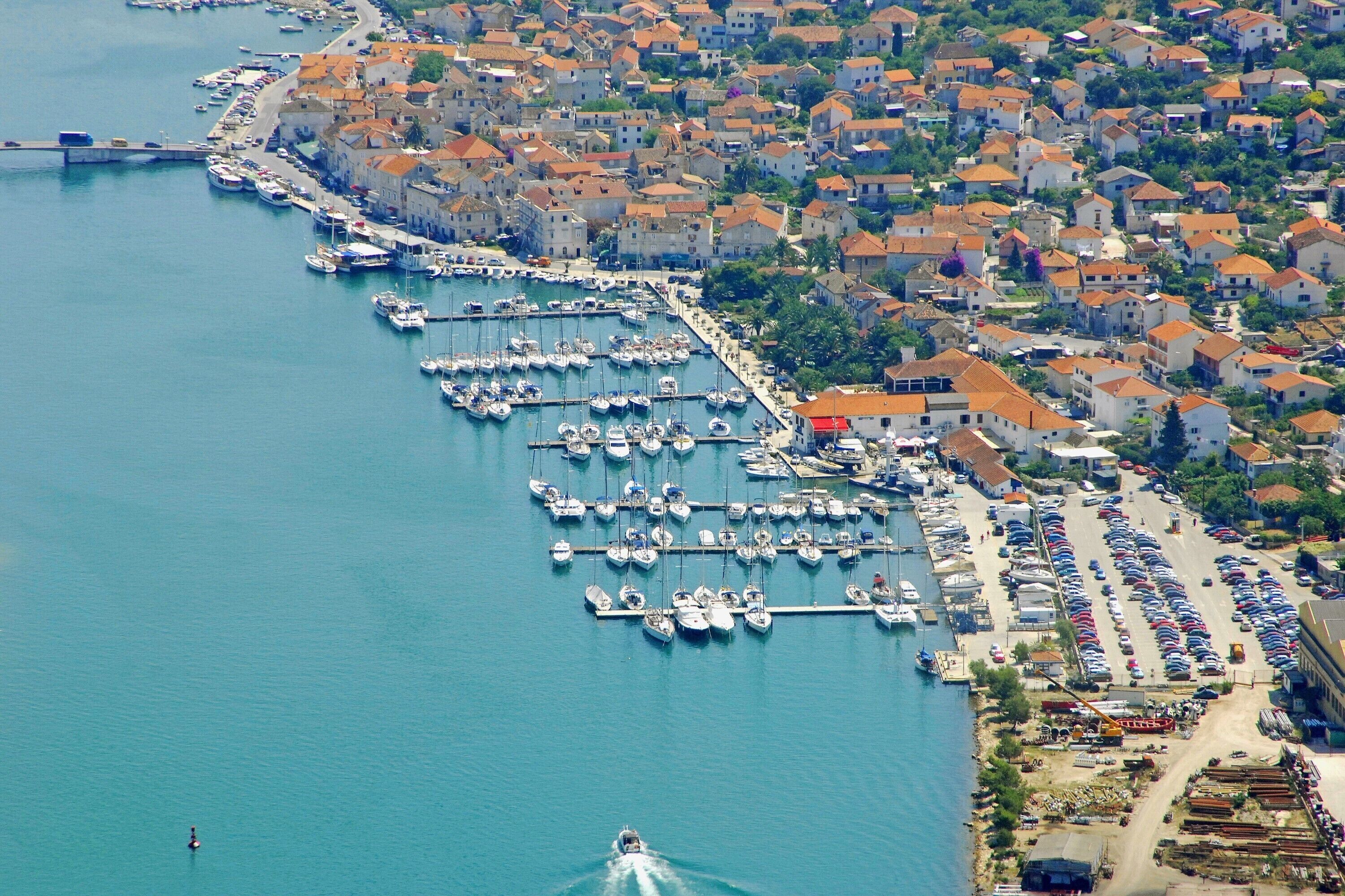 An aerial view of a coastal town with a marina, boats, and buildings.