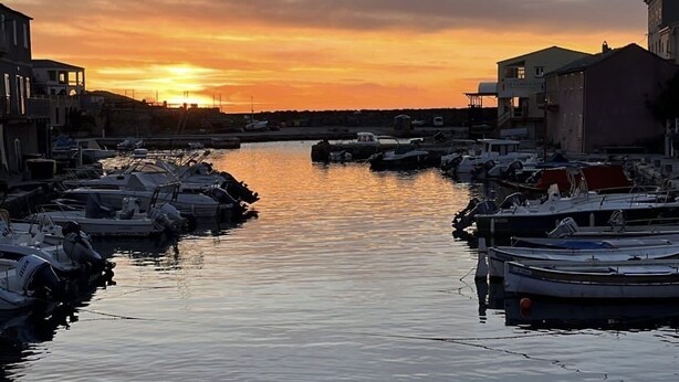 A marina with boats docked, a sunset in the background, and buildings on either side. - Studio 30 m2 Dans Petit Port de Pêche (Centuri)