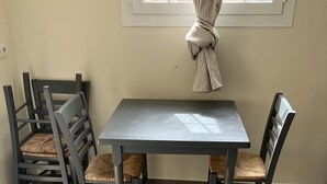 A dining area with a table and four chairs, a window with curtains, and tiled flooring. - Studio 30 m2 Dans Petit Port de Pêche (Centuri)
