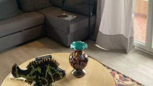 A living room with a sofa, a small table with a dinosaur figurine, a lamp, and two paintings on the wall. - Appartement rez de Chaussée (Mandelieu-la-Napoule)