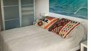 A bedroom with a bed, pillows, a wardrobe, and a large wave painting on the wall. - Appartement rez de Chaussée (Mandelieu-la-Napoule)