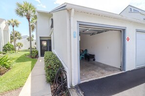 Een woon garage met huisnummer 26, een overdekte parkeerplaats en een kleine tuin met palmboompjes en struiken.