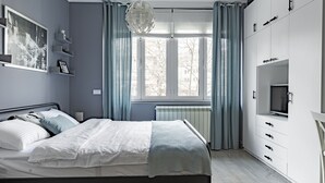 Moderni makuuhuone, jossa on sänky, lipasto, televisio ja ikkuna, jossa on verhot.