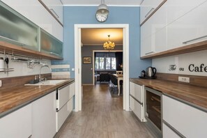 Une cuisine moderne avec des armoires blanches, des plans de travail en bois et une horloge bien visible au mur.