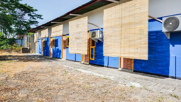 Une rangée de bâtiments bleus avec de grandes fenêtres et des portes, dont certains sont dotés de stores en bambou, et un appareil de climatisation sur le côté droit.