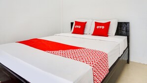 Un lit avec une couvre-lit à motifs rouges et blancs, deux oreillers rouges sur lesquels est inscrit le mot « oyo », et un matelas blanc.
