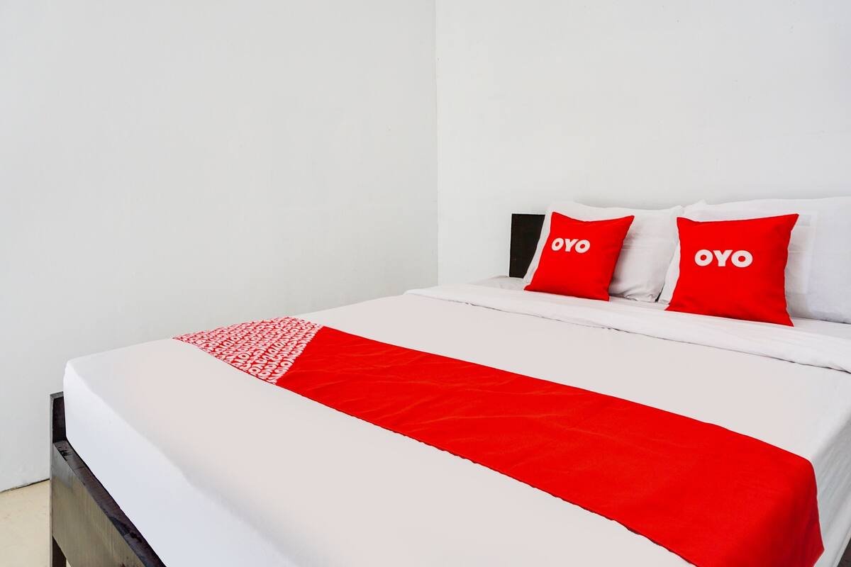 Een bed met witte beddengoed en rode accenten, waaronder kussens en een deken.